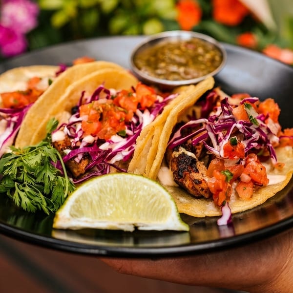 Three vibrant tacos with red cabbage, salsa, cilantro, and lime, held on a black plate.